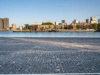 the man is riding his bike near the city with buildings in the background and a lake behind him