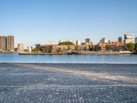 the man is riding his bike near the city with buildings in the background and a lake behind him