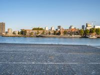 the man is riding his bike near the city with buildings in the background and a lake behind him