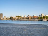 the man is riding his bike near the city with buildings in the background and a lake behind him
