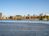 the man is riding his bike near the city with buildings in the background and a lake behind him