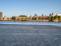 the man is riding his bike near the city with buildings in the background and a lake behind him