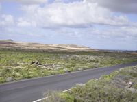 the man on his bike is riding down the road near the ocean and mountains in the distance