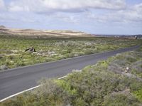 the man on his bike is riding down the road near the ocean and mountains in the distance