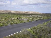 the man on his bike is riding down the road near the ocean and mountains in the distance