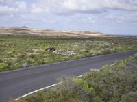 the man on his bike is riding down the road near the ocean and mountains in the distance