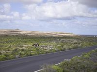 the man on his bike is riding down the road near the ocean and mountains in the distance