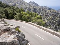 a man riding a bike down the road on top of a mountain side overlooking a rocky cliff