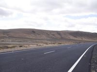 a man riding down the middle of a country road on an asphalt road surrounded by hills