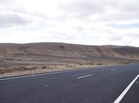 a man riding down the middle of a country road on an asphalt road surrounded by hills