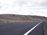 a man riding down the middle of a country road on an asphalt road surrounded by hills