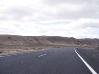 a man riding down the middle of a country road on an asphalt road surrounded by hills