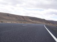 a man riding down the middle of a country road on an asphalt road surrounded by hills