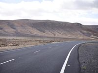 a man riding down the middle of a country road on an asphalt road surrounded by hills