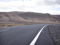 a man riding down the middle of a country road on an asphalt road surrounded by hills