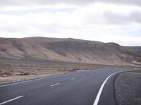a man riding down the middle of a country road on an asphalt road surrounded by hills