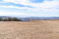 a man riding on the side of a dirt road with trees in the distance and hills in the background