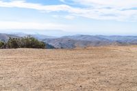 a man riding on the side of a dirt road with trees in the distance and hills in the background