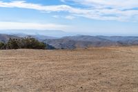 a man riding on the side of a dirt road with trees in the distance and hills in the background