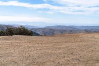 a man riding on the side of a dirt road with trees in the distance and hills in the background