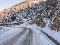 a man riding a horse in the snow past a rocky cliff on a country road