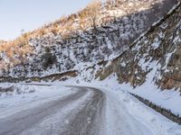 a man riding a horse in the snow past a rocky cliff on a country road