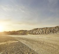 a man riding his motorcycle on a dirt road in front of mountains and sky at sunset