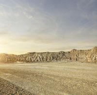 a man riding his motorcycle on a dirt road in front of mountains and sky at sunset