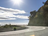 a man on his motorcycle rides along an empty road in the sunlight and it looks nice