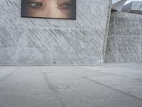 man with hat on skateboard riding across concrete sidewalk near building with sign on wall