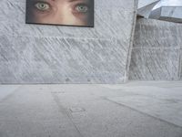 man with hat on skateboard riding across concrete sidewalk near building with sign on wall