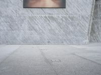 man with hat on skateboard riding across concrete sidewalk near building with sign on wall