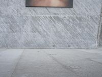 man with hat on skateboard riding across concrete sidewalk near building with sign on wall