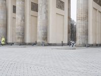 a man sits on a bench in an empty square between large stone pillars on top of snow covered ground