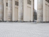 a man sits on a bench in an empty square between large stone pillars on top of snow covered ground