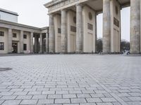 a man sits on a bench in an empty square between large stone pillars on top of snow covered ground