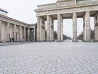 a man sits on a bench in an empty square between large stone pillars on top of snow covered ground