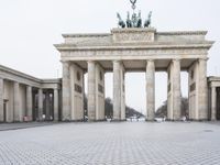 a man sits on a bench in an empty square between large stone pillars on top of snow covered ground