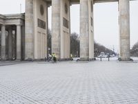a man sits on a bench in an empty square between large stone pillars on top of snow covered ground