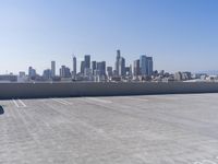 a man is sitting on top of a building with his skateboard in hand, and the view of a city is very wide