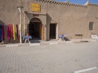 the man is sitting in front of his shop in the city street, while holding his hands to his knee