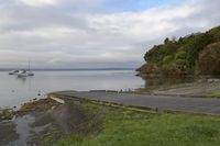 a man is sitting next to the water by a dock on a cloudy day with a boat