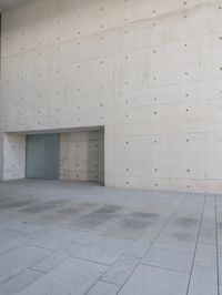 a man on a skateboard stands outside of an empty building and looks out from a glass entrance