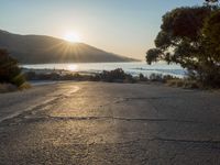 a man is riding his skateboard on the road near the water and mountains during a sunny day