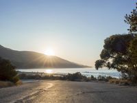 a man is riding his skateboard on the road near the water and mountains during a sunny day