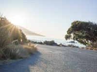 a man is riding his skateboard on the road near the water and mountains during a sunny day