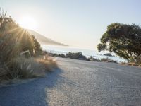 a man is riding his skateboard on the road near the water and mountains during a sunny day