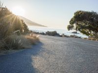 a man is riding his skateboard on the road near the water and mountains during a sunny day
