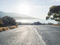a man is riding his skateboard on the road near the water and mountains during a sunny day