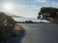 a man is riding his skateboard on the road near the water and mountains during a sunny day